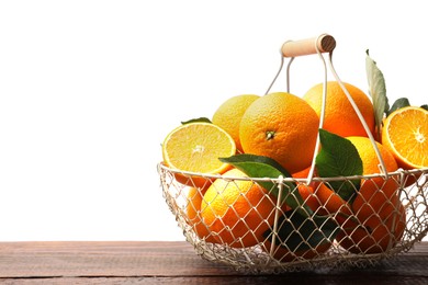 Photo of Juicy oranges and green leaves in metal basket on wooden table against white background. Space for text