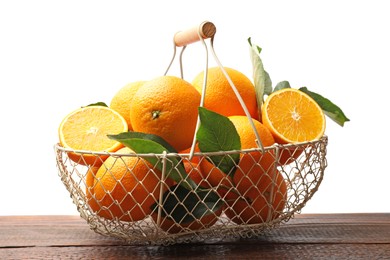 Photo of Juicy oranges and green leaves in metal basket on wooden table against white background