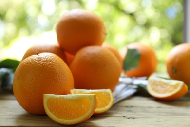 Photo of Fresh whole and cut oranges on wooden table against blurred green background, closeup