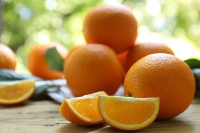 Photo of Fresh whole and cut oranges on wooden table against blurred green background, closeup