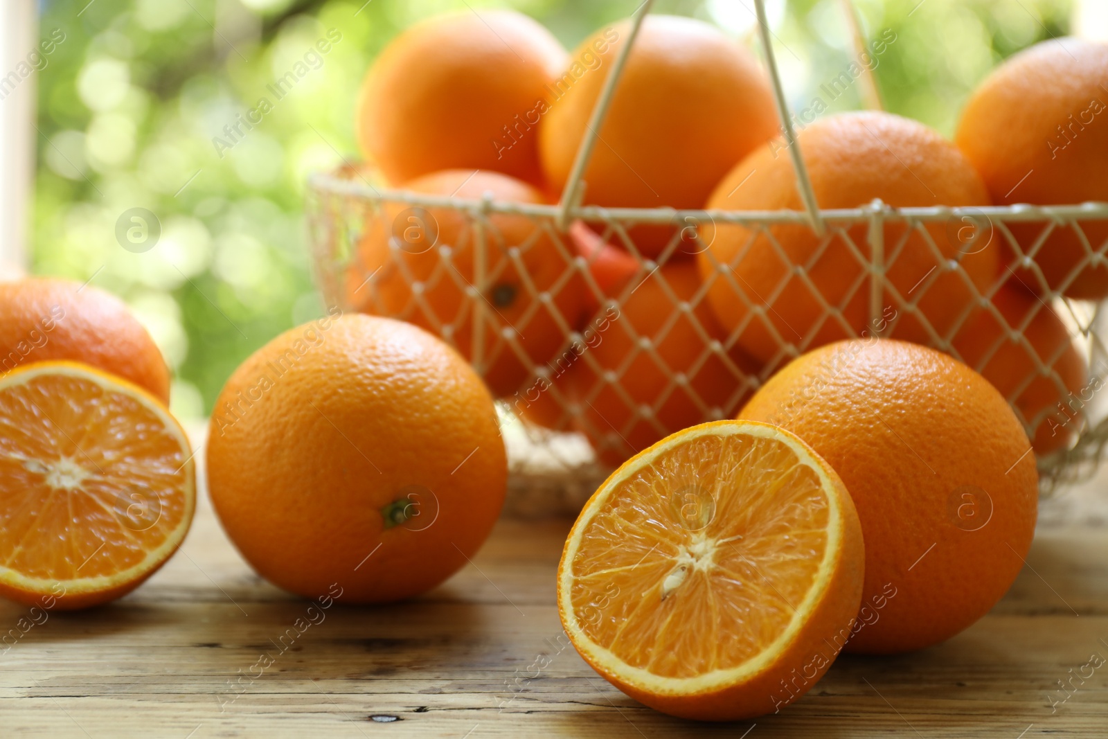 Photo of Fresh whole and cut oranges on wooden table against blurred green background, closeup