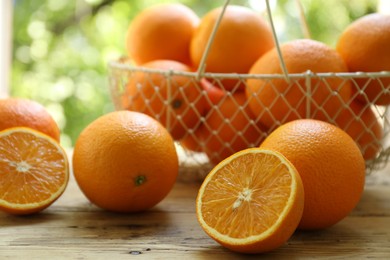 Photo of Fresh whole and cut oranges on wooden table against blurred green background, closeup