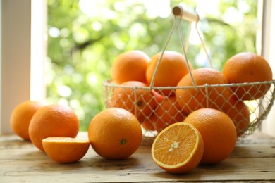 Photo of Fresh whole and cut oranges on wooden table against blurred green background, closeup