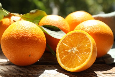 Photo of Fresh whole and cut oranges on wooden table against blurred green background, closeup