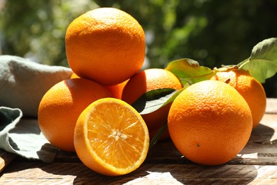Photo of Fresh whole and cut oranges on wooden table against blurred green background, closeup