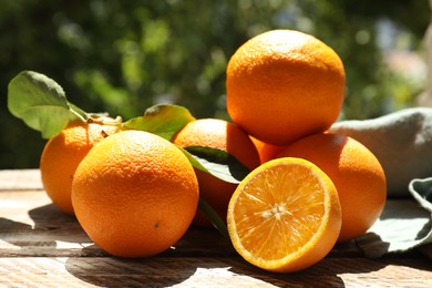 Photo of Fresh whole and cut oranges on wooden table against blurred green background, closeup