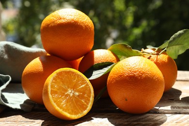 Photo of Fresh whole and cut oranges on wooden table against blurred green background, closeup