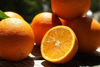 Photo of Fresh whole and cut oranges on wooden table against blurred background, closeup