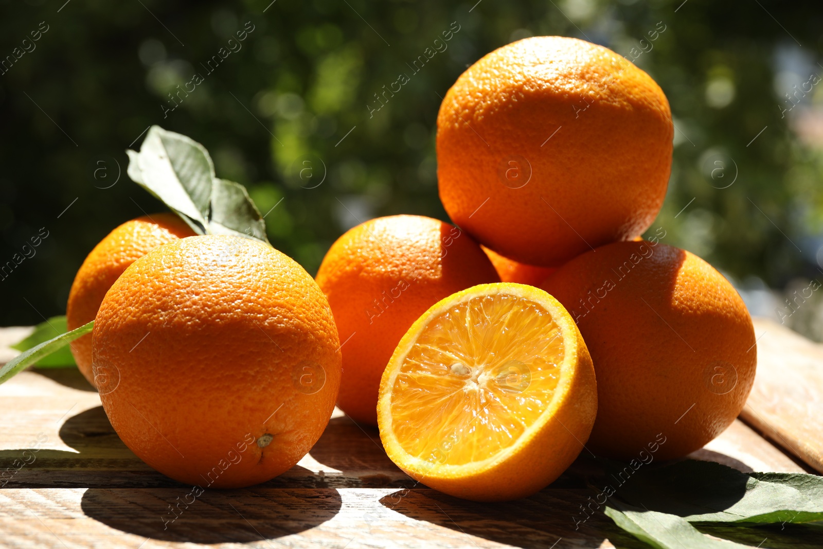 Fresh whole and cut oranges on wooden table against blurred green background, closeup Photo of Fresh whole and cut oranges on wooden table against blurred green background, closeup