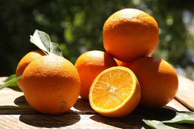 Photo of Fresh whole and cut oranges on wooden table against blurred green background, closeup