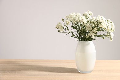 Photo of Beautiful flowers in vase on wooden table against grey background, space for text