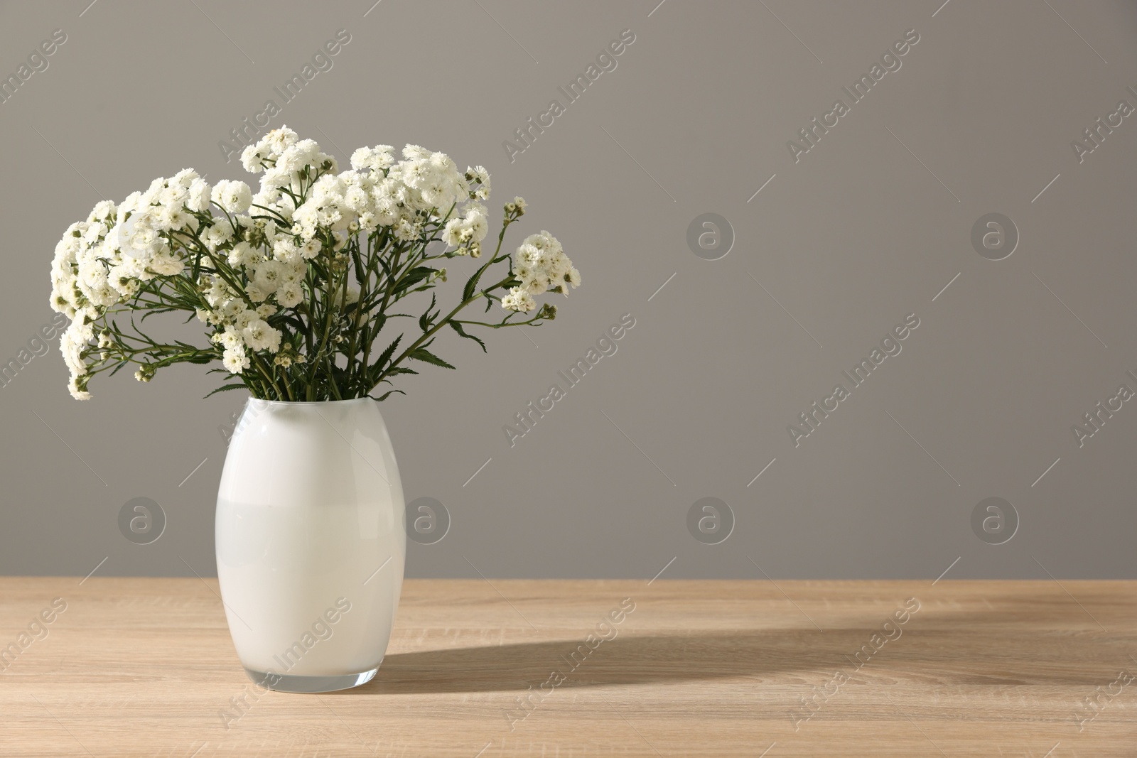 Beautiful flowers in vase on wooden table against grey background, space for text Photo of Beautiful flowers in vase on wooden table against grey background, space for text