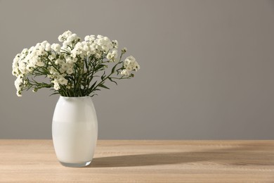 Photo of Beautiful flowers in vase on wooden table against grey background, space for text