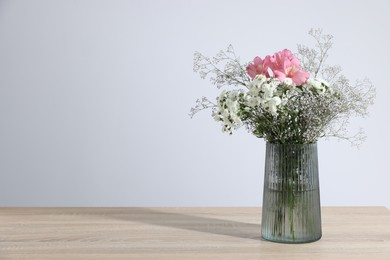 Photo of Beautiful flowers in vase on wooden table against white background, space for text