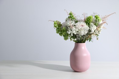 Photo of Beautiful flowers in vase on white table, space for text