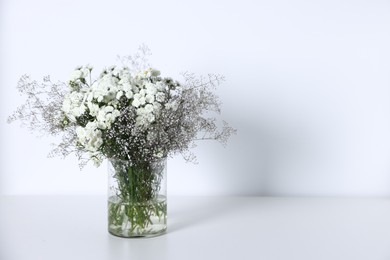 Photo of Beautiful flowers in vase on white table, space for text