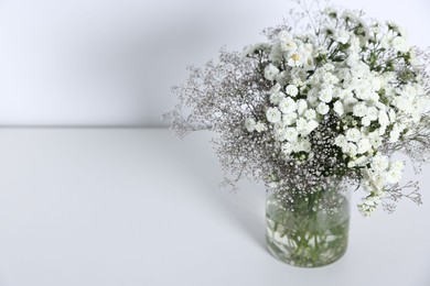 Photo of Beautiful flowers in vase on white table, space for text