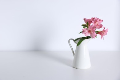 Photo of Beautiful flowers in vase on white table, space for text