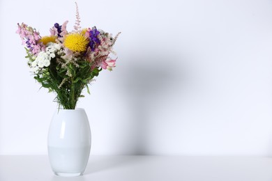 Photo of Beautiful flowers in vase on white table, space for text