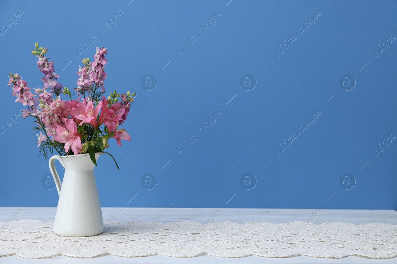 Photo of Beautiful flowers in vase on white wooden table against light blue background, space for text