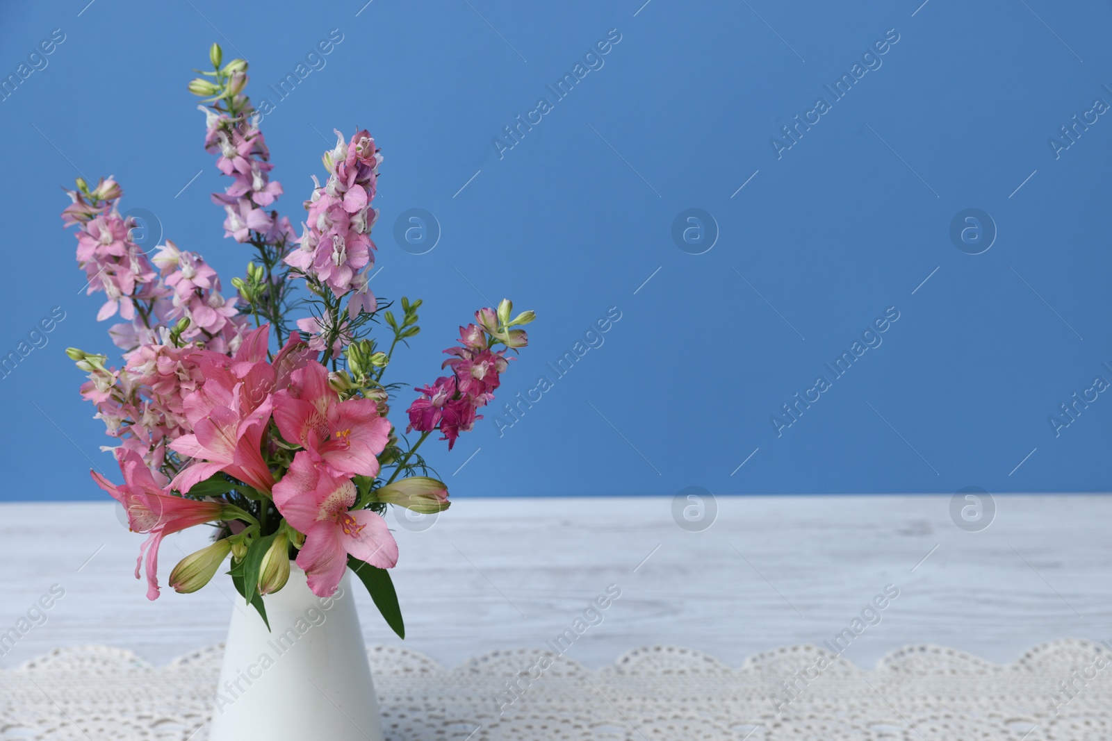 Photo of Beautiful flowers in vase on white wooden table against light blue background, closeup. Space for text