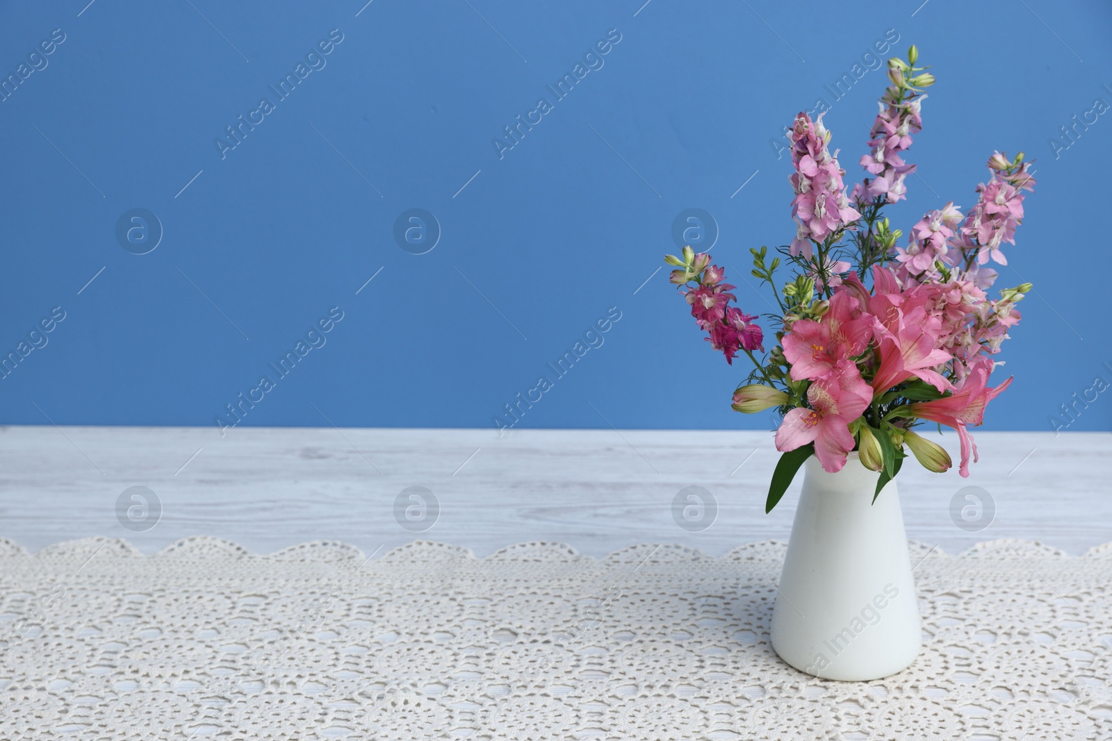 Photo of Beautiful flowers in vase on white wooden table against light blue background, space for text