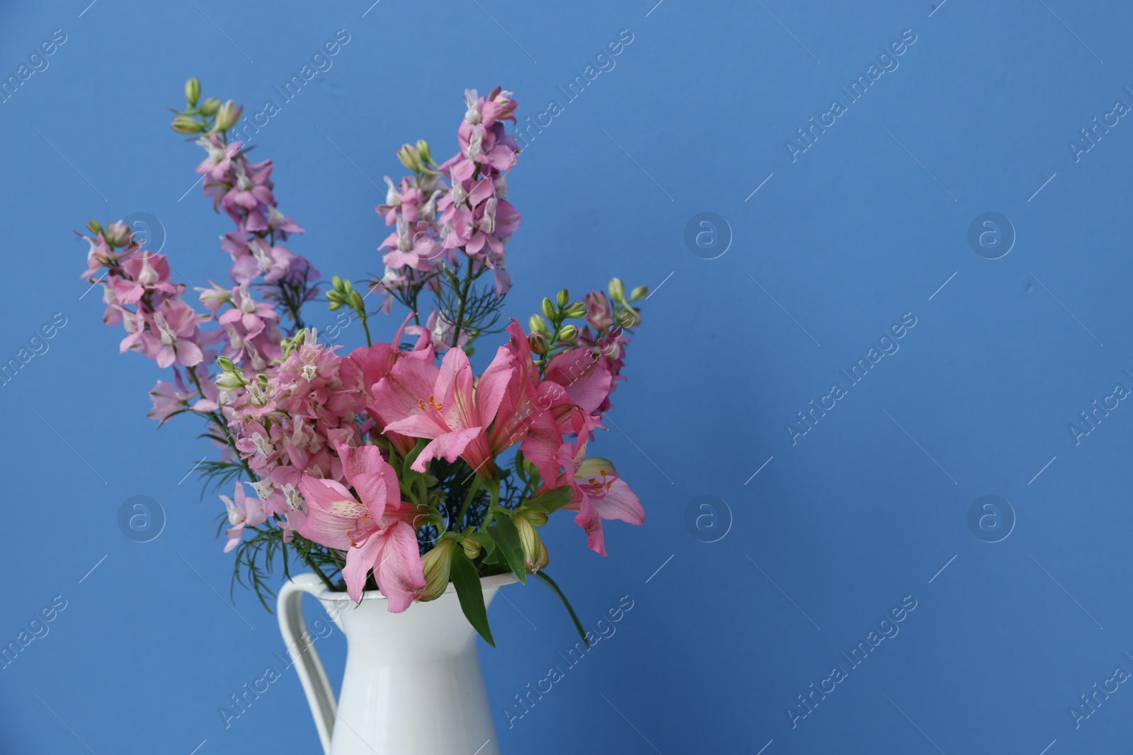 Photo of Beautiful flowers in vase on light blue background, closeup. Space for text