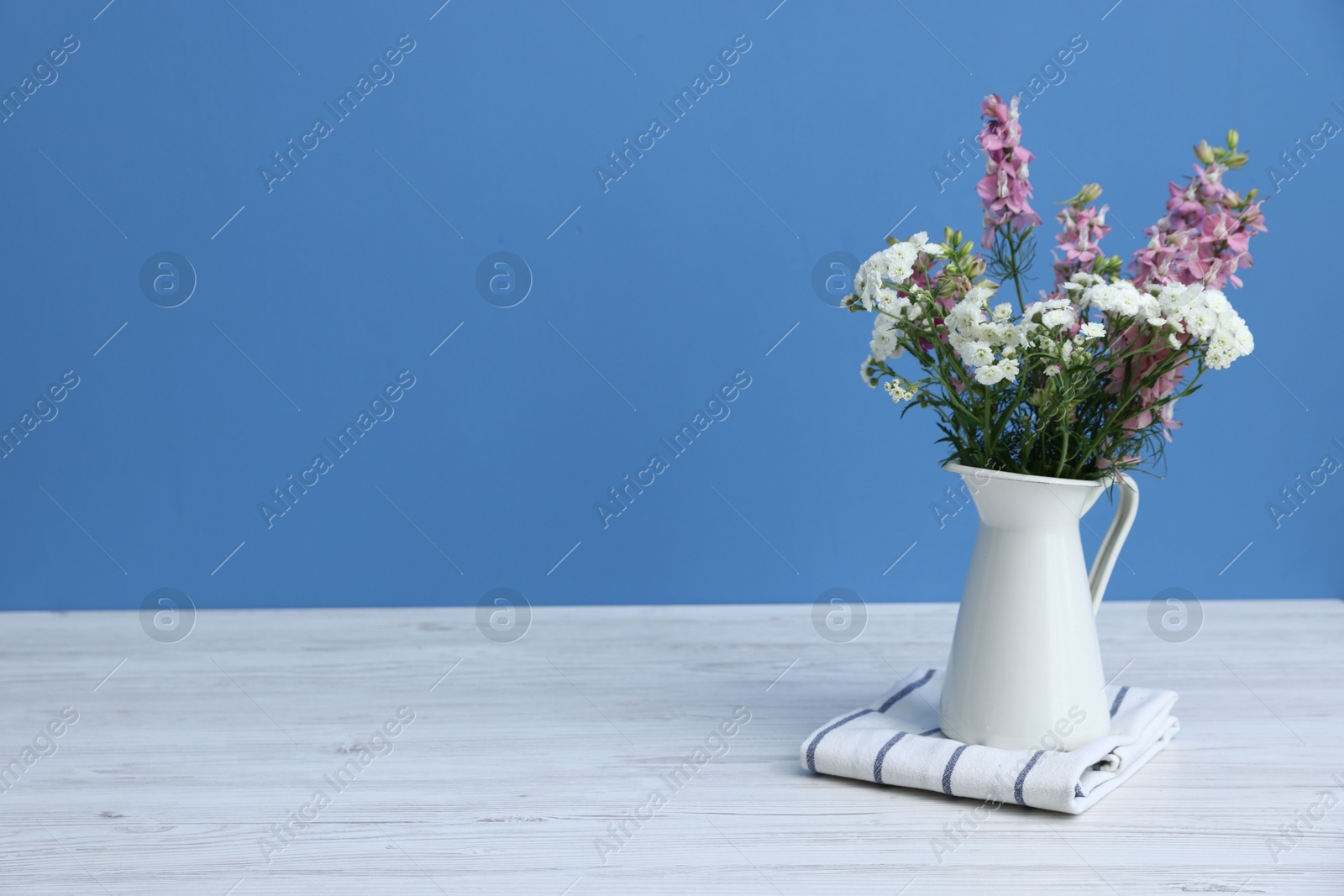 Photo of Beautiful flowers in vase on white wooden table against light blue background, space for text