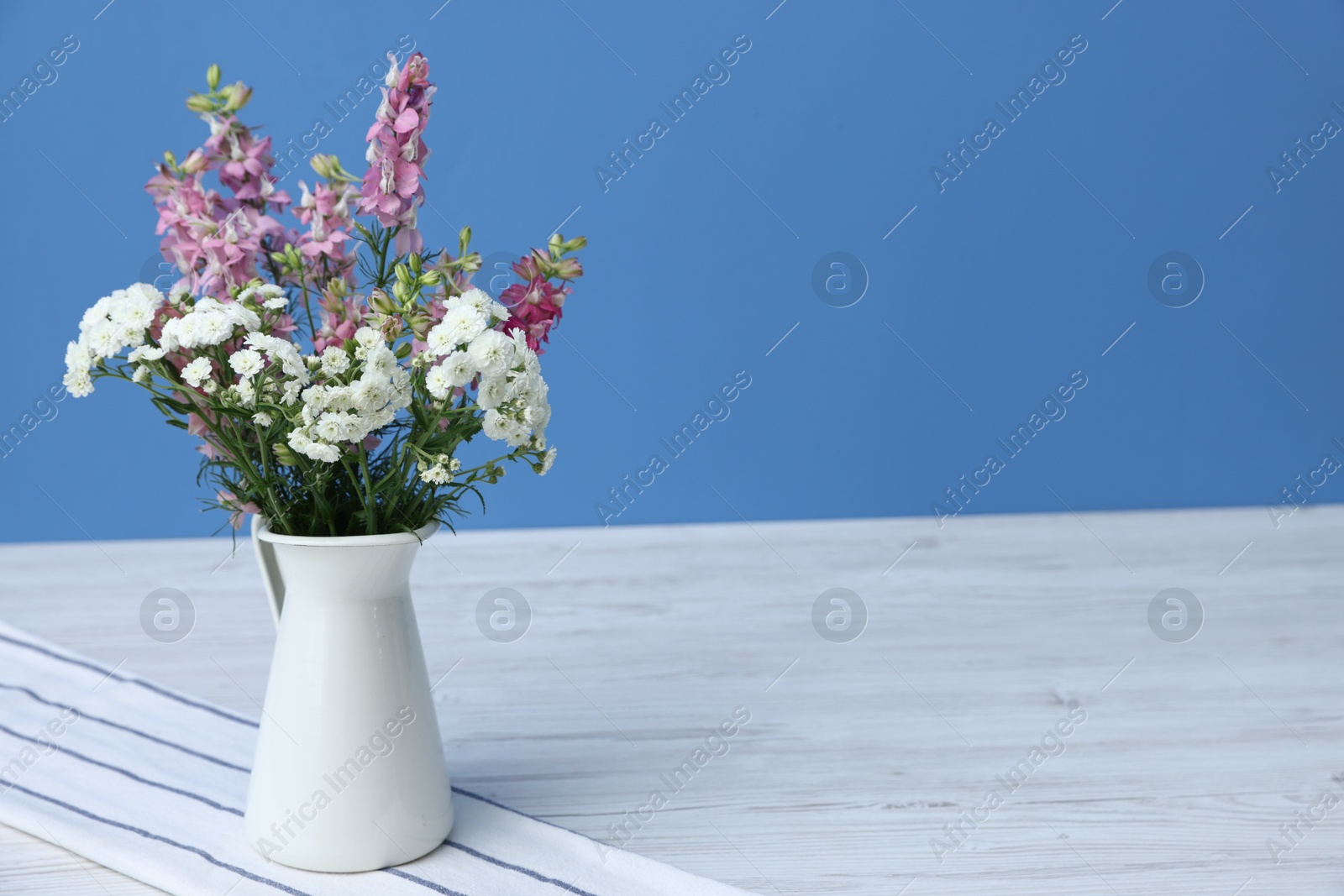 Photo of Beautiful flowers in vase on white wooden table against light blue background, space for text