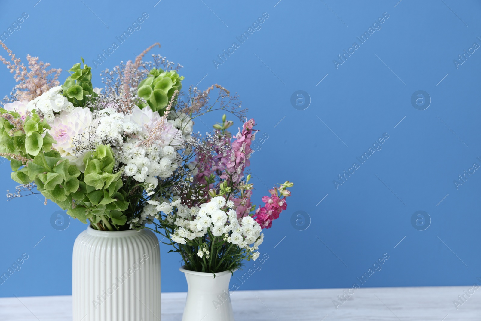 Beautiful flowers in vases on white wooden table against light blue background, closeup. Space for text Photo of Beautiful flowers in vases on white wooden table against light blue background, closeup. Space for text