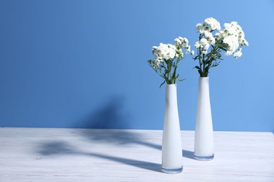 Photo of Beautiful flowers in vases on white wooden table against light blue background, space for text