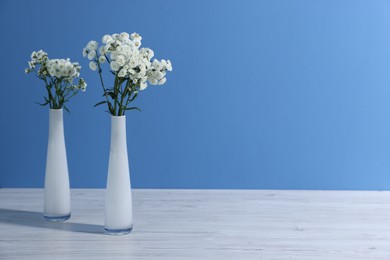 Photo of Beautiful flowers in vases on white wooden table against light blue background, space for text