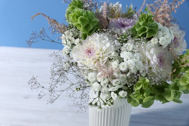 Photo of Beautiful flowers in vase on white wooden table against light blue background, closeup