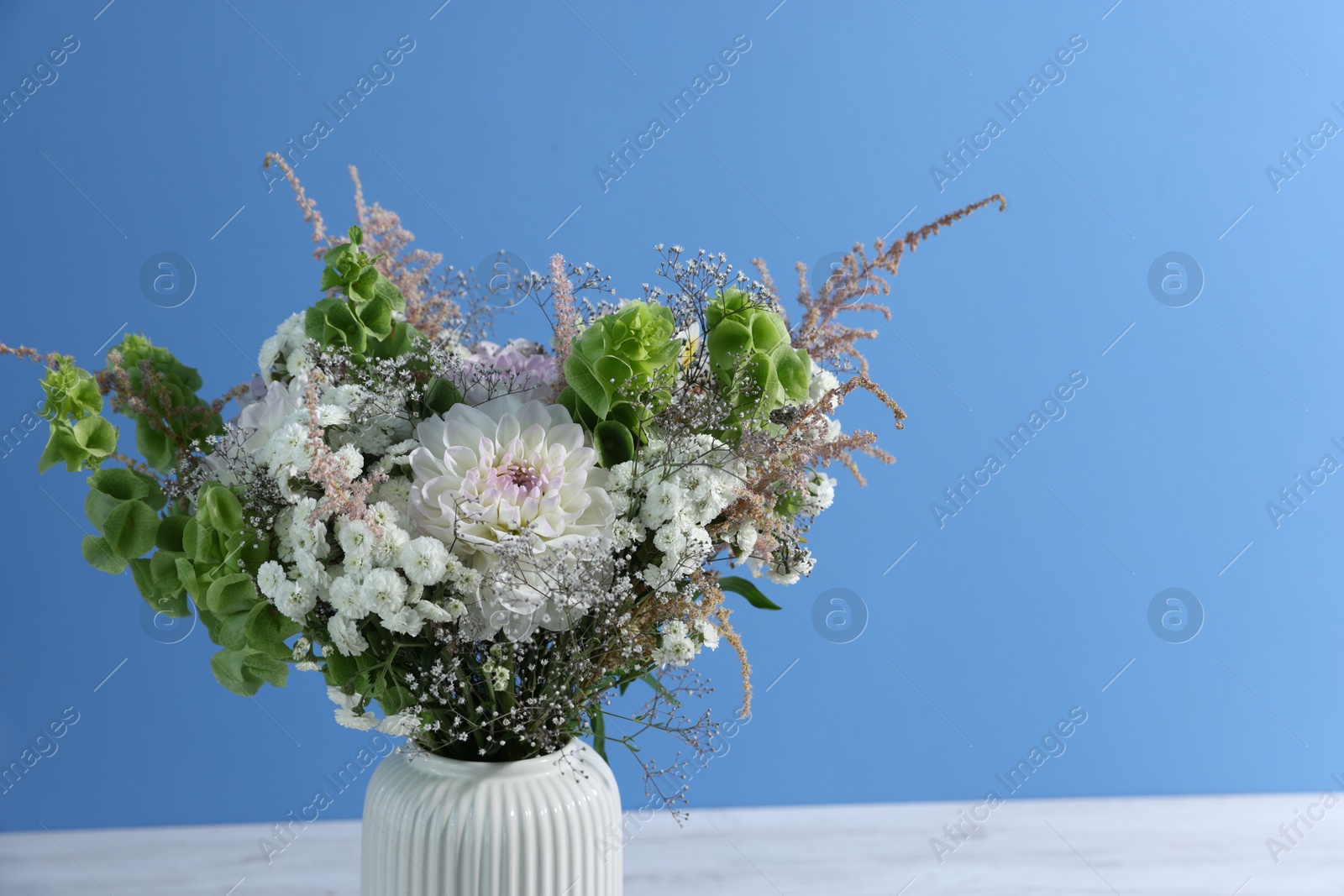 Beautiful flowers in vase on white table against light blue background, closeup. Space for text Photo of Beautiful flowers in vase on white table against light blue background, closeup. Space for text