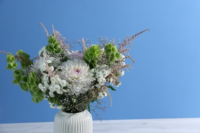 Photo of Beautiful flowers in vase on white table against light blue background, closeup. Space for text