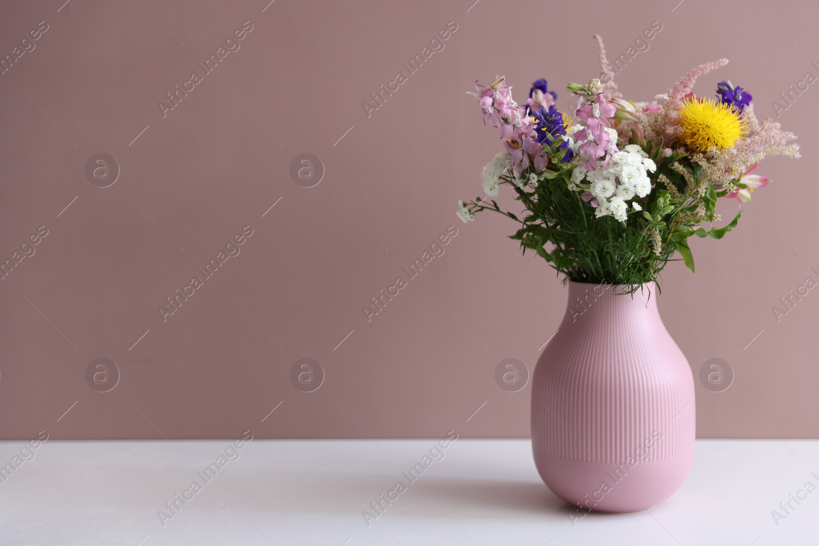 Beautiful flowers in vase on white table against pink background, space for text Photo of Beautiful flowers in vase on white table against pink background, space for text