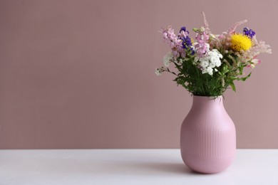 Photo of Beautiful flowers in vase on white table against pink background, space for text