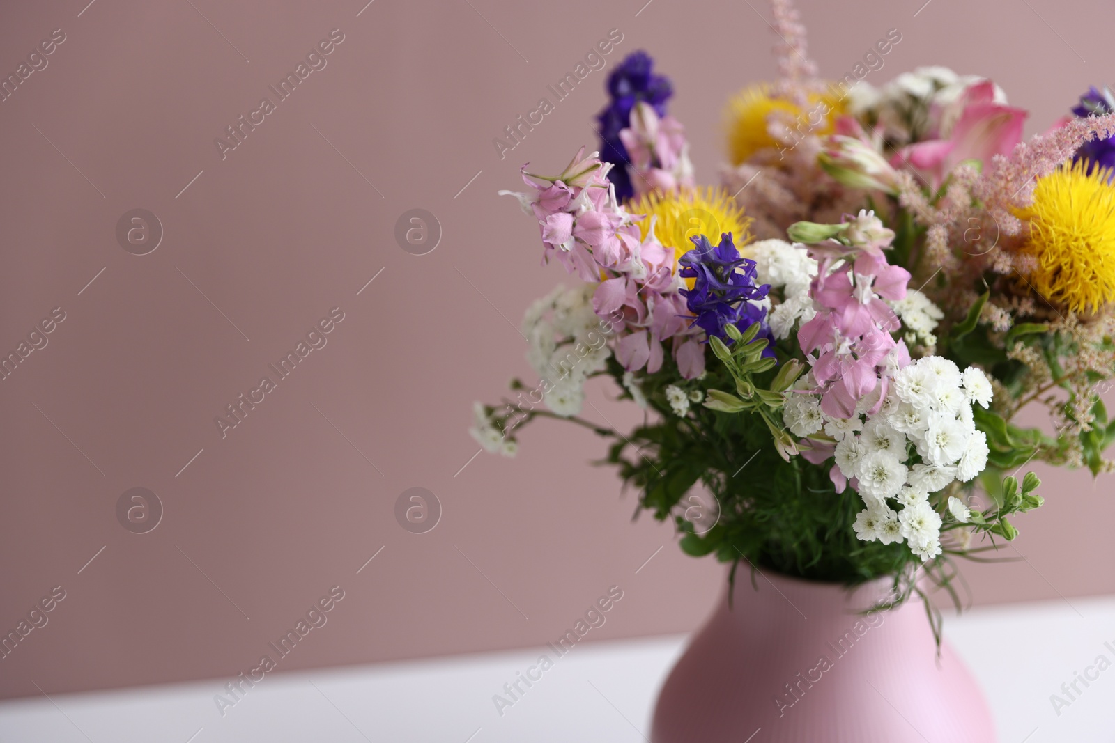 Beautiful flowers in vase on white table against pink background, closeup. Space for text Photo of Beautiful flowers in vase on white table against pink background, closeup. Space for text