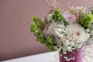 Photo of Beautiful flowers in vase on white table against pink background, closeup. Space for text