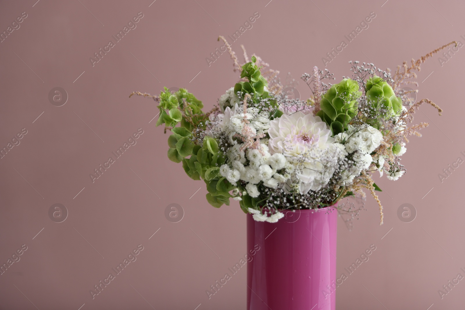 Photo of Beautiful flowers in vase on pink background, closeup. Space for text