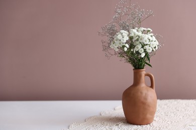Photo of Beautiful flowers in vase on white table against pink background, space for text