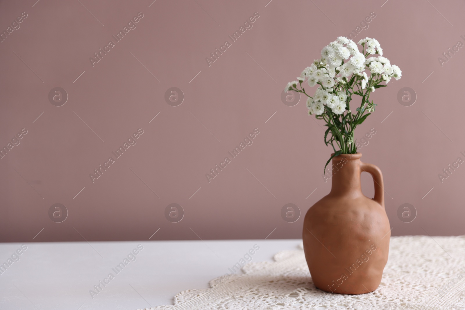 Photo of Beautiful flowers in vase on white table against pink background, space for text
