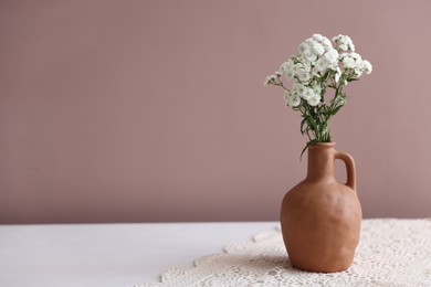 Photo of Beautiful flowers in vase on white table against pink background, space for text