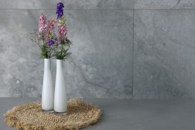 Photo of Beautiful flowers in vases on grey table, space for text