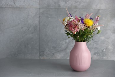 Photo of Beautiful flowers in vase on grey table, space for text