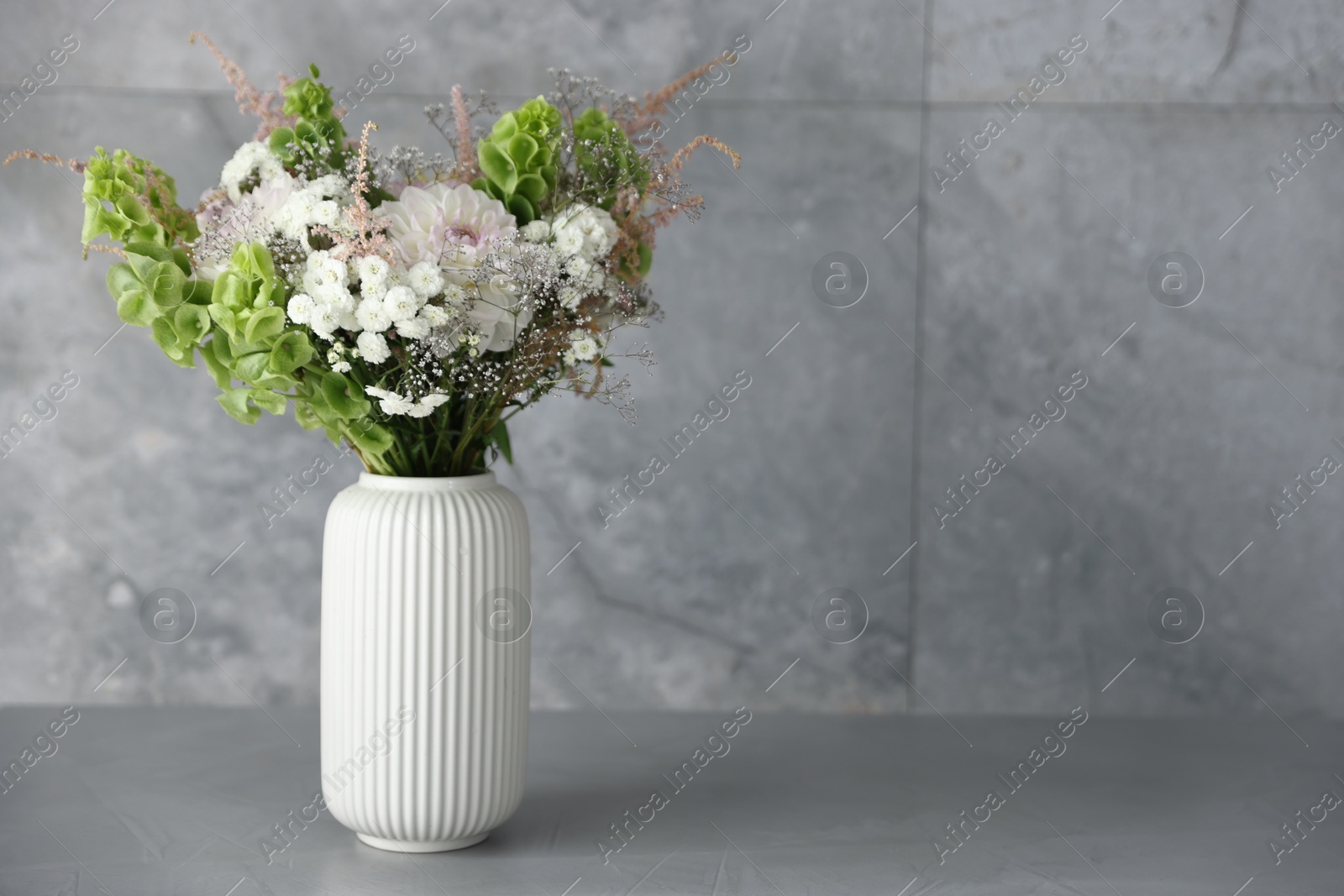 Beautiful flowers in vase on grey table, space for text Photo of Beautiful flowers in vase on grey table, space for text