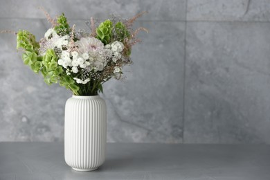 Photo of Beautiful flowers in vase on grey table, space for text