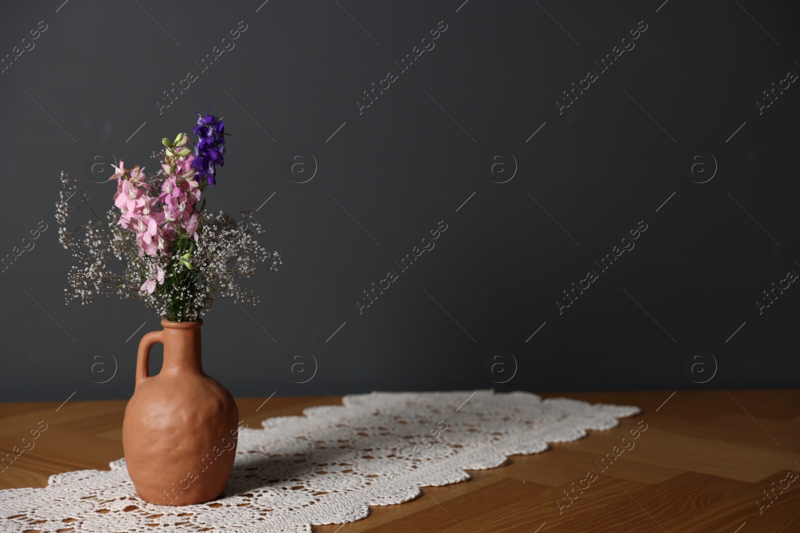 Beautiful flowers in vase on wooden table against dark grey background, space for text Photo of Beautiful flowers in vase on wooden table against dark grey background, space for text