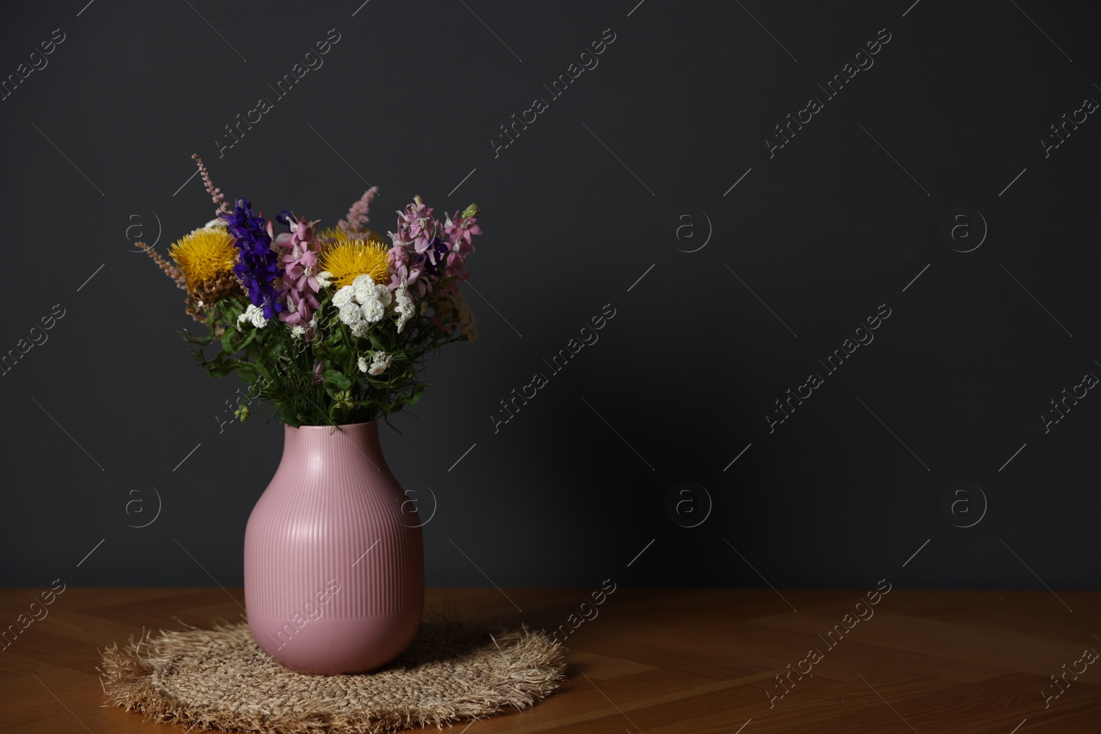Beautiful flowers in vase on wooden table against dark grey background, space for text Photo of Beautiful flowers in vase on wooden table against dark grey background, space for text