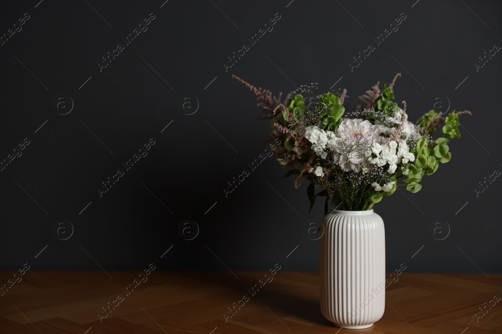Beautiful flowers in vase on wooden table against dark grey background, space for text Photo of Beautiful flowers in vase on wooden table against dark grey background, space for text